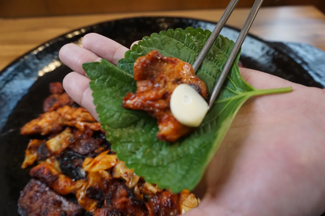 깻잎에 직화 닭갈비와 마늘을 올려 싸 먹는 모습