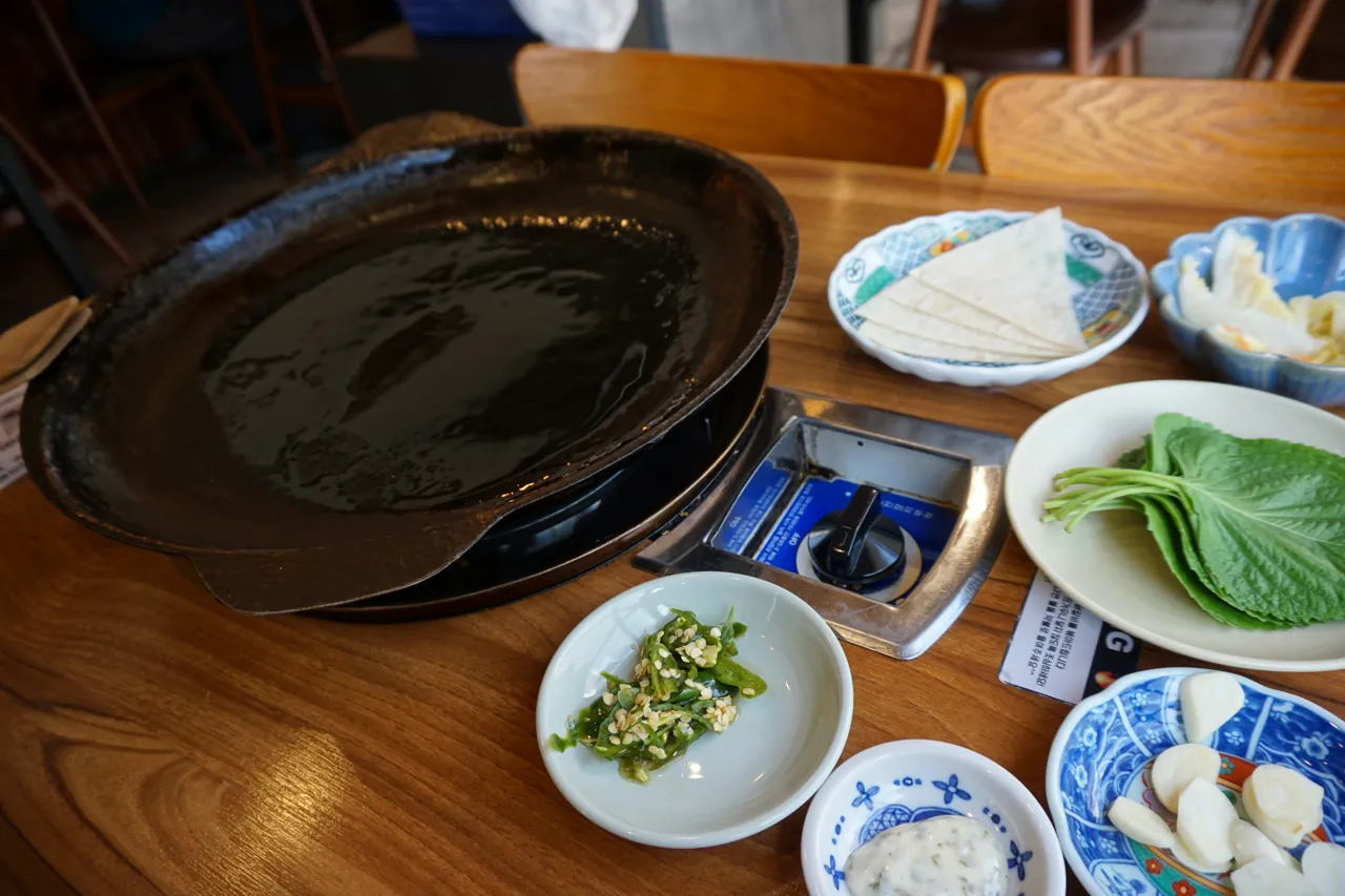 무쇠 철판과 깻잎, 쌈무, 반찬이 차려진 테이블